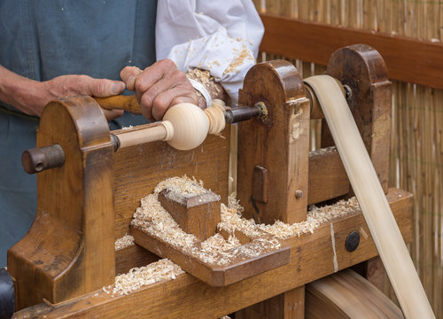 An artisan carves a piece of wood using an old manual lathe