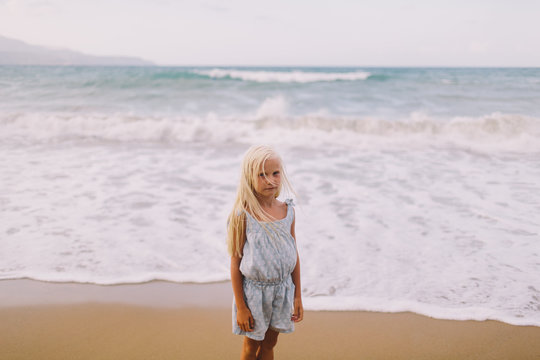 Little blond girl looking into the camera standing on the seashore
