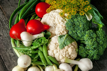 Mixed vegetables of cauliflower and broccoli, garlic, green onions, tomatoes and green peas on a wooden background in rustic style for Thanksgiving.