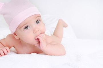 Cute baby lying on a white bedsheet and keeps fingers in his mouth