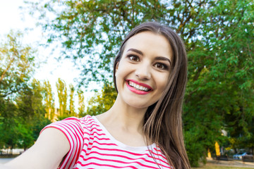 Pretty smiling girl making selfie, long-haired brunette in white clothes, closeup