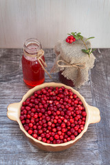 Very ripe cowberry in a bowl on the table and red bilberry beverage and jam. On a wooden background, space for text.