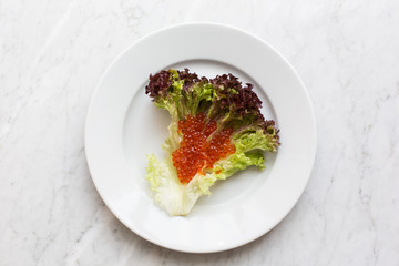 Top view of red caviar on a salad leaf on a light marble background. copy space, Top view
