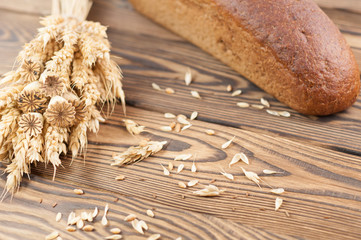 One bundle of wheat and poppy and lot of scattered grain and single whole bread on old rustic wooden planks