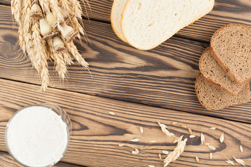 One bundle of wheat and poppy and lot of scattered grain and slices of bread and flour in glass on old rustic wooden planks