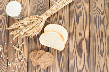 One bundle of wheat and poppy and lot of scattered grain and slices of bread and flour in glass on old rustic wooden planks