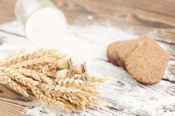 One bundle of wheat and poppy and flour poured out of glass and slices of bread on old rustic wooden planks
