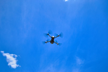 Flight of a gray quadrocopter against a blue sky.