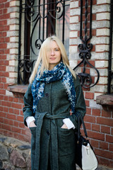 Красивая девушка со светлыми волосами стоит в пальто, на шее объемный шарф. Стильная девушка в пальто
