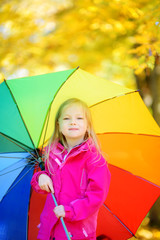 Cute little girl holding rainbow umbrella on beautiful autumn day. Happy child playing in autumn park.