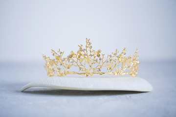 Golden crown on a white ceramic plate on grey background, close-up