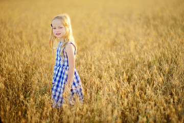 Adorable girl walking happily in wheat field on warm and sunny summer evening