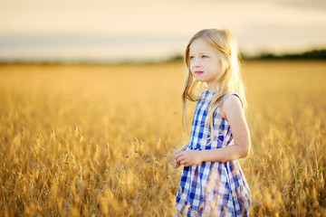 Adorable girl walking happily in wheat field on warm and sunny summer evening
