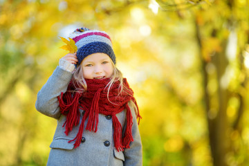 Cute little girl having fun on beautiful autumn day. Happy child playing in autumn park. Kid gathering yellow fall foliage.