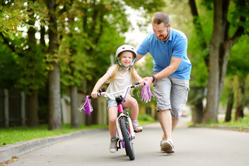 Happy father teaching his little daughter to ride a bicycle. Child learning to ride a bike.