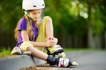 Pretty little girl learning to roller skate on beautiful summer day in a park