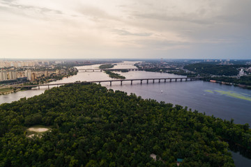 Fototapeta na wymiar Panoramic view of Kiev city with the Dnieper River in the middle. Aerial view of the residential district and industrial Zone at sunset. Two banks of the river connected by bridges