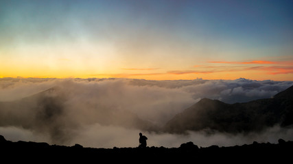Fototapeta premium The Photographer Taking Pictures on the Mountain with Clouds During Sunset/Sunrise