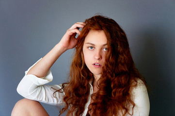 Model tests. Beautiful redhead girl with curly hair. Natural color. portrait on a grey background. Studio