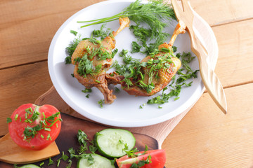 Roasted duck legs with cucumbers, tomatoes and herbs on a white plate