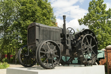 An old black wheeled tractor stands as a monument on a white pedestal closeup