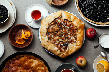 Variety of autumn pies: blueberry tart, chantarelle galette and classical apple pie with sweet pastry crust. Harvest time baking concept. Concrete rustic background.