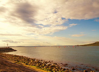 Obraz premium Photo of a beautiful scenic sea landscape. Yachts in sea, view on Howth Harbour Lighthouse, Howth Peninsula, county Dublin, Ireland. Lightly toned