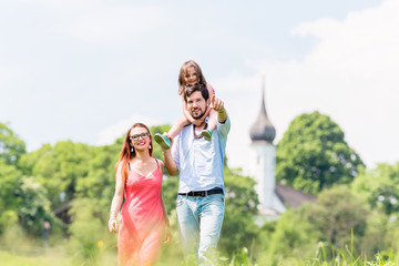 Fototapeta premium Family walking on meadow having walk, dad is carrying his little daughter on the shoulders