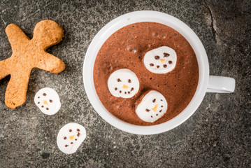 Traditional Christmas drink idea. Hot chocolate mug with marshmallow, decorated in the form of snowmen, On black stone table top view copy space