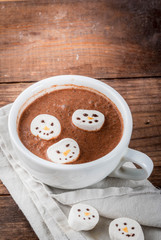Traditional Christmas drink idea. Hot chocolate mug with marshmallow, decorated in the form of snowmen, On wooden table copy space