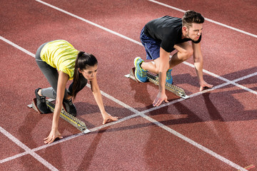 Male and female athlete in starting position at starting block of cinder track