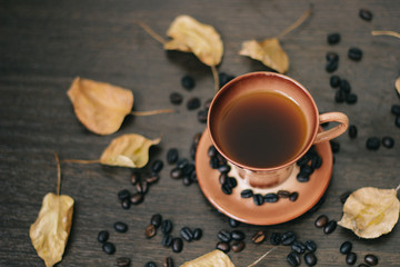 a cup of black coffee in the mug, surrounded by autumn leaves and coffee beans, top view.