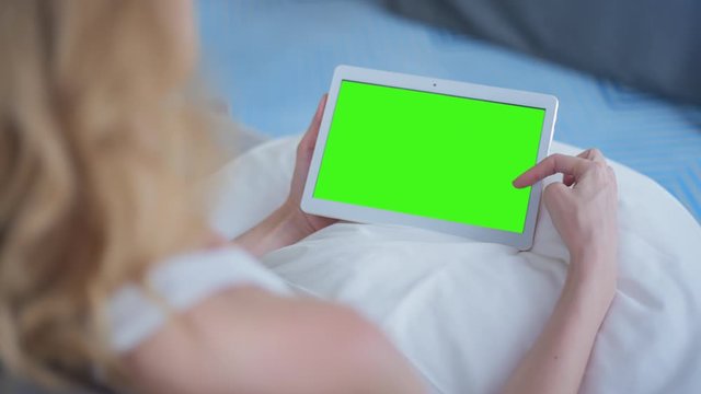 Young Woman in white top sitting on couch uses Tablet PC with pre-keyed green screen. Few types of gestures - scrolling up and down, tapping, zoom in and out. Perfect for screen compositing