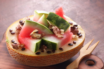 Melon stuffed with watermelon, sprinkled with walnut on a wooden board