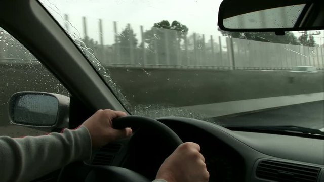 Driving on highway on a rainy day. Hand on steering wheel POV