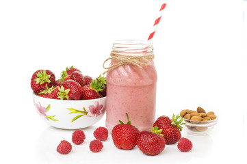 Pink strawberry and raspberry smoothie in a mason jar glass with straw and scattered berries