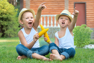 Two brothers sitting on the grass and eat corn on the cob in the garden.Fun games,laughter.