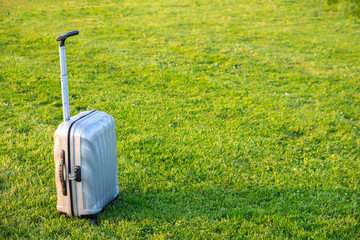 Modern silver suitcase in green grass on natural background.