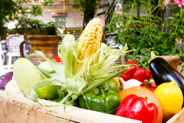 Different vegetables and fruits: orange, lemon, corn, eggplant, peppers, zucchini lying in a wooden box. The new harvest.