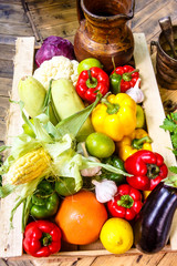 Different vegetables and fruits: orange, lemon, corn, eggplant, peppers, zucchini lying in a wooden box. The new harvest.