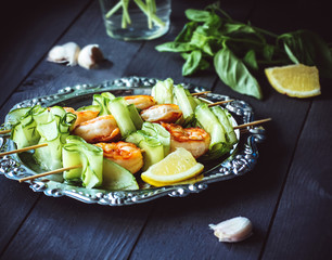 Shrimps with skewers, on a silver plate with lemon, basil and garlic. On a dark wooden background.
