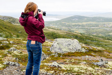 Young adult Caucasian woman taking photographs of mountainous landscape on a foggy summer day.