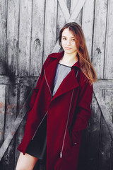 Long-haired trendy girl dressed up in red coat and black skirt standing in front of the wooden door