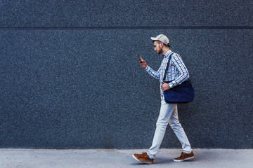 Young urban casual businessman walking and reading messages on smartphone