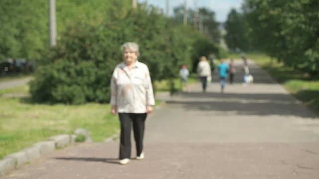 Elderly woman walking in the park in summer. Slow motion