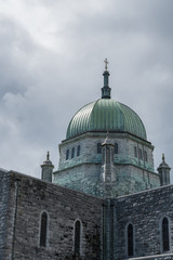Obraz premium Galway, Ireland - August 5, 2017: Outside view of green dome with cross of the Cathedral under dark skies. Gray stone walls of the church.