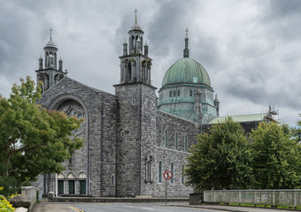 Galway, Ireland - August 5, 2017: Outside view of the Cathedral with green dome, main entrance at nave flanked by two towers. Street scene with green trees on sides.