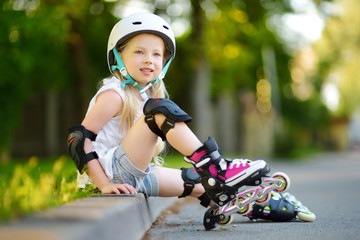 Pretty little girl learning to roller skate on beautiful summer day in a park