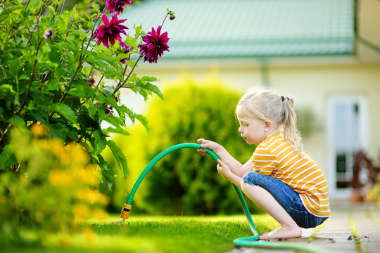 Cute little girl watering flowers in the garden at summer day.