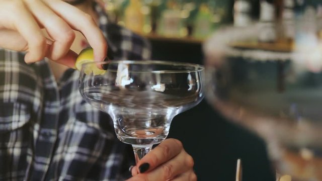 Bar cocktail drinks concept - closeup of glass greasing by lime lemon acid, young female barmen making mix alcohol tequila margarita cocktails mexican atmosphere